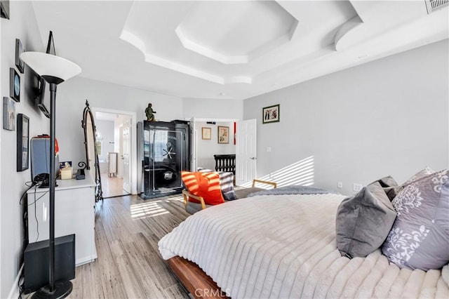 bedroom featuring light wood-style flooring, visible vents, and a raised ceiling