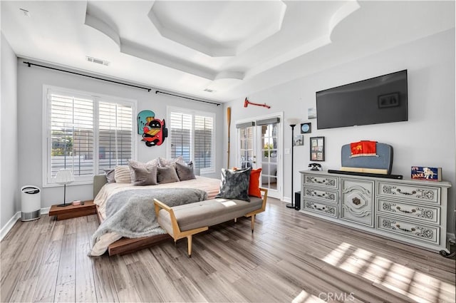 bedroom with multiple windows, a tray ceiling, visible vents, and light wood-type flooring