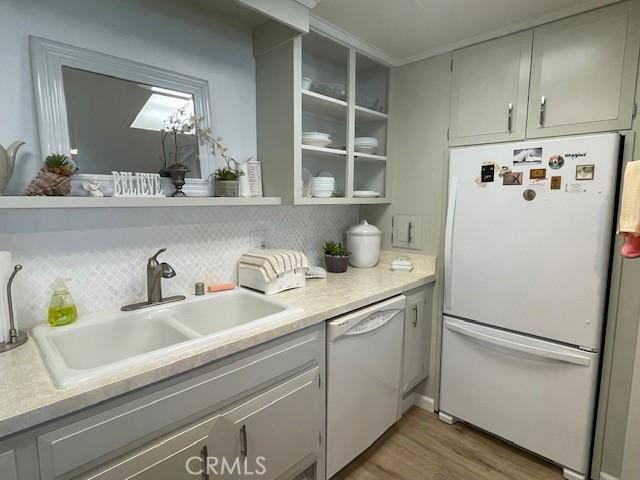 kitchen featuring light countertops, decorative backsplash, light wood-style flooring, white appliances, and a sink