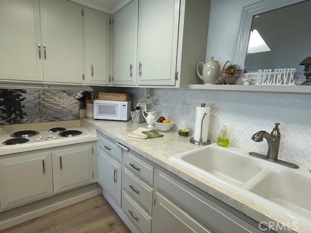 kitchen featuring light wood-style flooring, a sink, white appliances, light countertops, and decorative backsplash