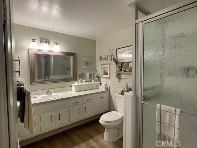 bathroom with toilet, a stall shower, vanity, and wood finished floors