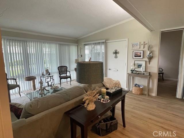 living room with vaulted ceiling, crown molding, light wood-type flooring, and baseboards