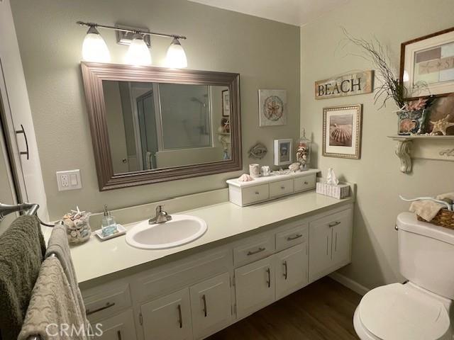 full bath featuring a shower with shower door, toilet, vanity, and wood finished floors