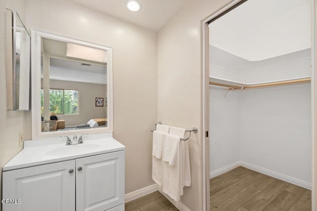 ensuite bathroom with a walk in closet, ensuite bath, wood finished floors, baseboards, and vanity