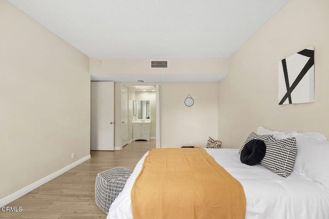 bedroom featuring ensuite bath, light wood-style flooring, baseboards, and visible vents