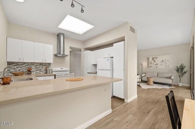 kitchen with white appliances, visible vents, light wood finished floors, a sink, and wall chimney range hood