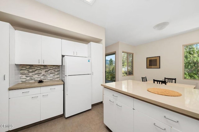 kitchen featuring decorative backsplash, white cabinetry, light countertops, and freestanding refrigerator