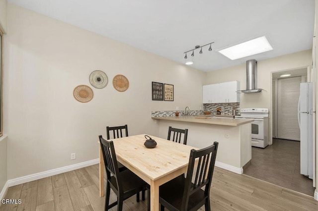 dining room with a skylight, light wood-style floors, and baseboards