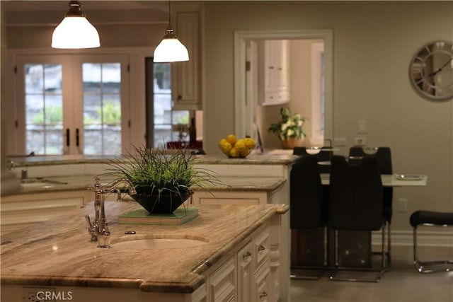 interior space with light stone countertops, pendant lighting, french doors, white cabinetry, and a sink