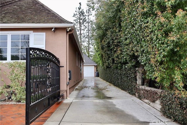 view of property exterior with stucco siding, a detached garage, an outbuilding, and a gate