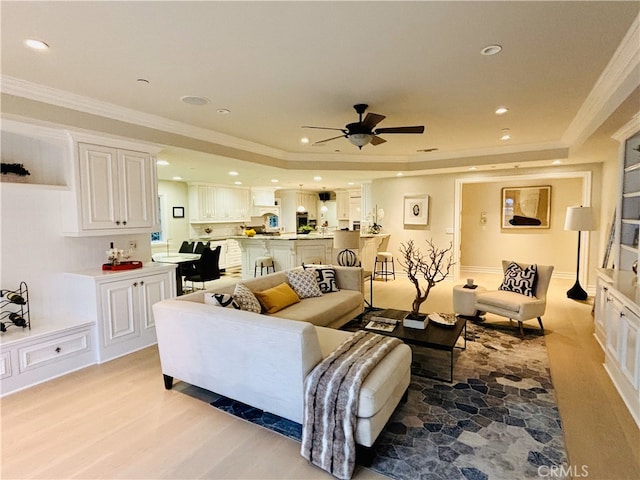 living area featuring crown molding, ceiling fan, a tray ceiling, light wood-style flooring, and recessed lighting