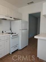 kitchen featuring under cabinet range hood, white appliances, white cabinets, and light countertops