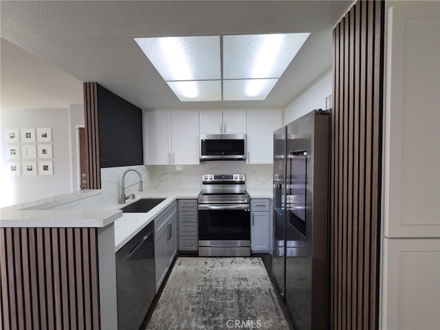 kitchen with a sink, light stone counters, backsplash, appliances with stainless steel finishes, and white cabinets