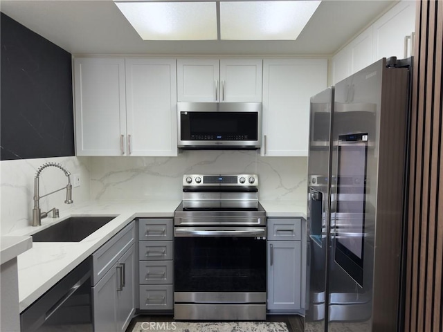 kitchen with a sink, light stone counters, gray cabinets, and stainless steel appliances