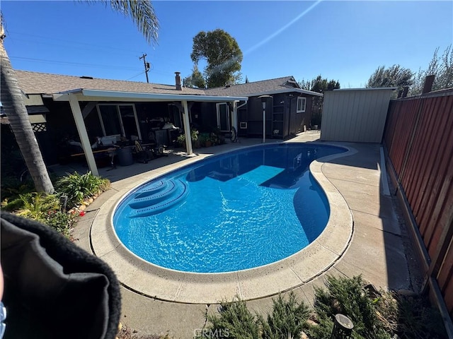 pool featuring an outbuilding, a shed, a patio area, and a fenced backyard