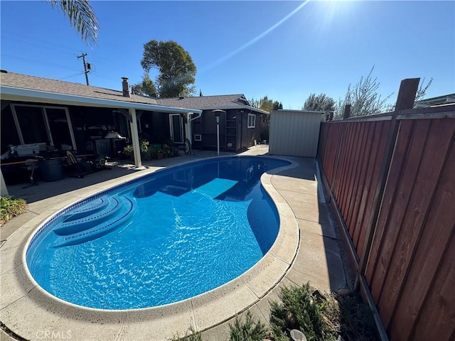 view of swimming pool featuring a fenced in pool, a shed, a fenced backyard, a patio area, and an outbuilding