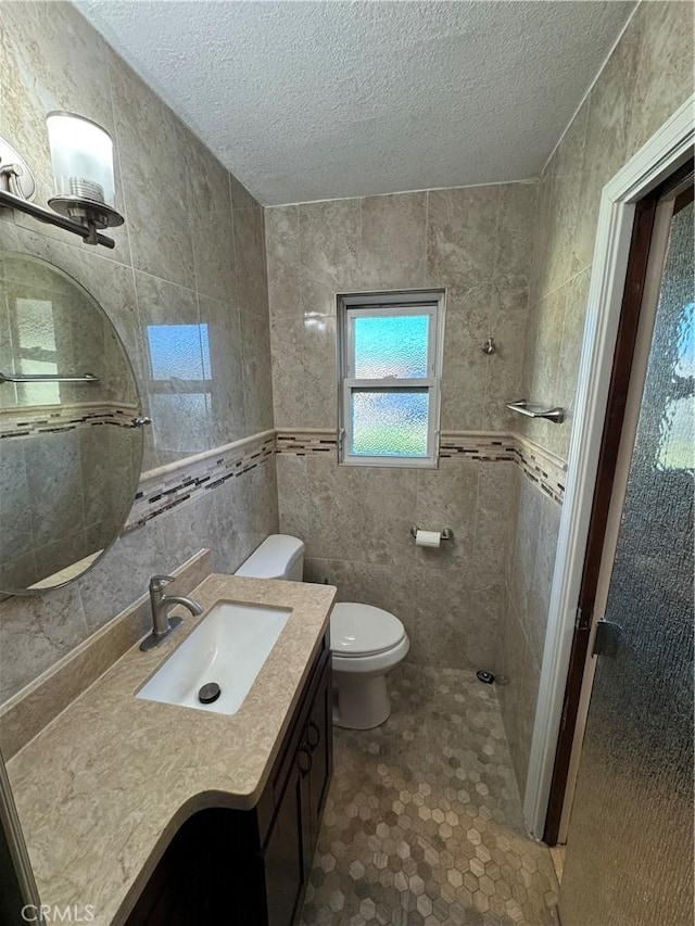 bathroom with toilet, vanity, a textured ceiling, and tile walls