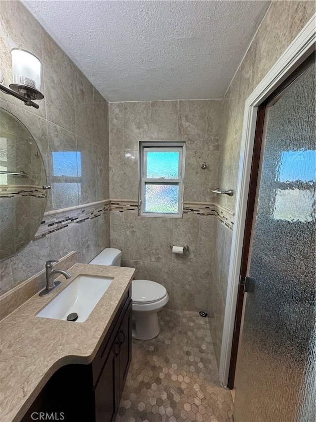 bathroom with toilet, tile walls, vanity, and a textured ceiling