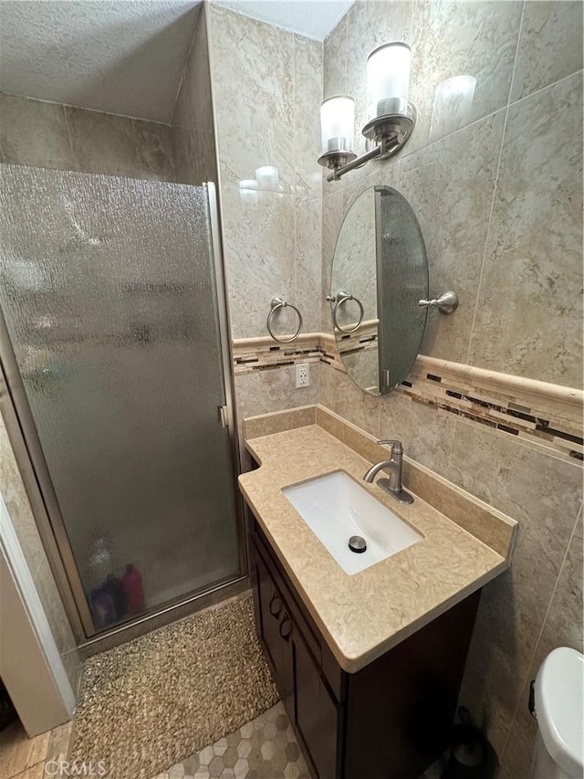 bathroom with vanity, a stall shower, a textured ceiling, tile walls, and toilet