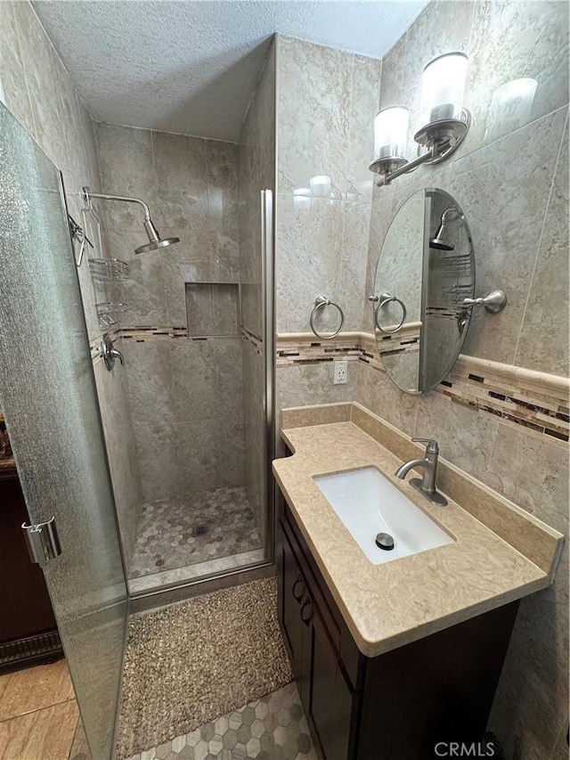 full bath with tasteful backsplash, a shower stall, tile walls, vanity, and a textured ceiling