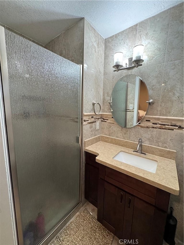 full bathroom with backsplash, a textured ceiling, tile walls, a shower stall, and vanity