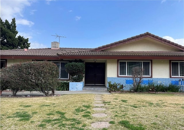 single story home with a front yard, a tiled roof, brick siding, and a chimney