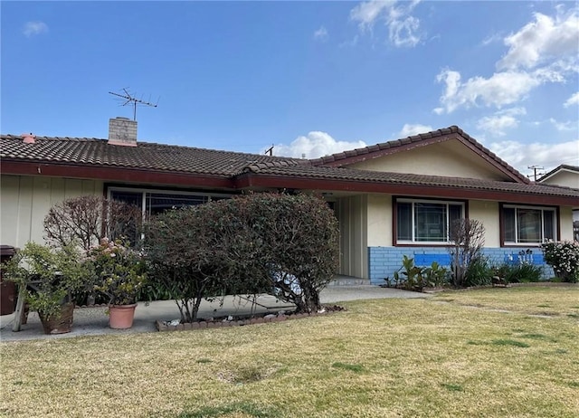 view of front of property featuring brick siding, a tiled roof, a chimney, and a front lawn