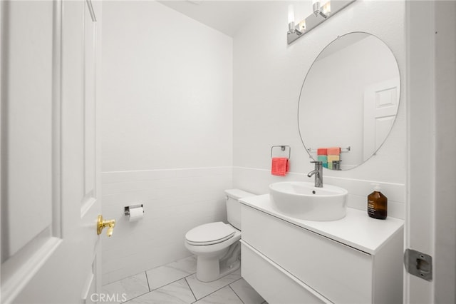 half bath featuring toilet, marble finish floor, vanity, and tile walls