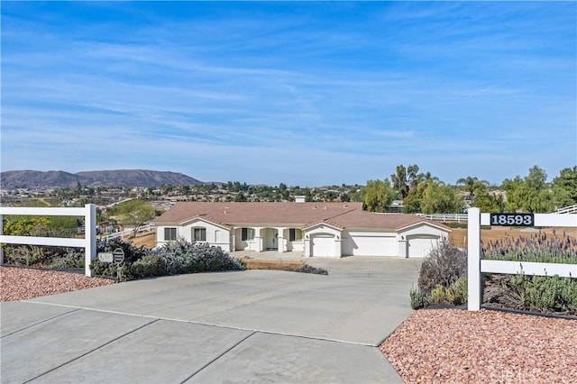 ranch-style home featuring an attached garage, fence, a mountain view, and driveway