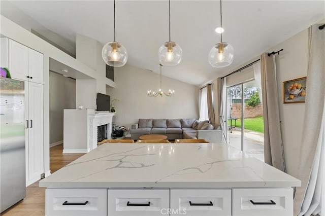 kitchen with a center island, vaulted ceiling, light stone counters, a fireplace, and stainless steel fridge