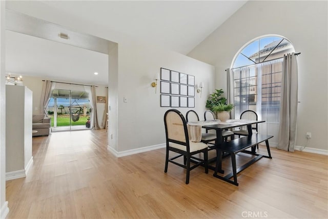 dining space featuring baseboards, light wood finished floors, and high vaulted ceiling