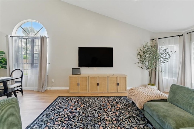 living area featuring vaulted ceiling, baseboards, and light wood finished floors