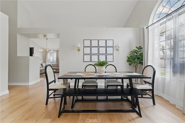 dining space featuring a healthy amount of sunlight, baseboards, light wood-type flooring, and an inviting chandelier