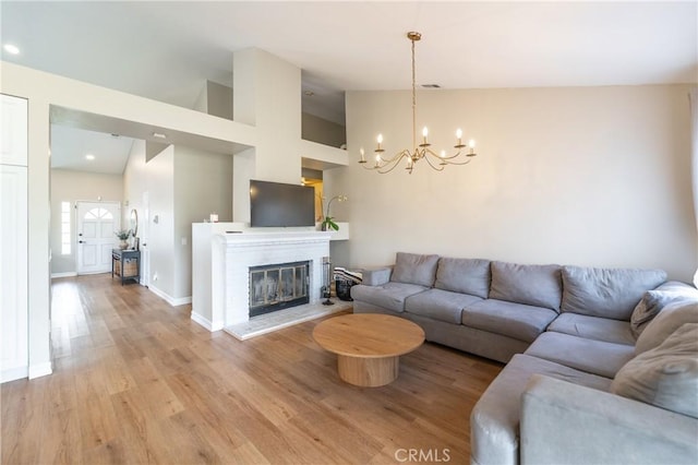 living area featuring light wood-type flooring, high vaulted ceiling, a glass covered fireplace, an inviting chandelier, and baseboards