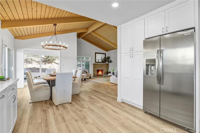 dining room with light wood-style flooring, vaulted ceiling with beams, a fireplace, wood ceiling, and a chandelier