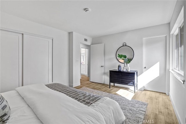 bedroom featuring a closet, visible vents, baseboards, and light wood-style floors