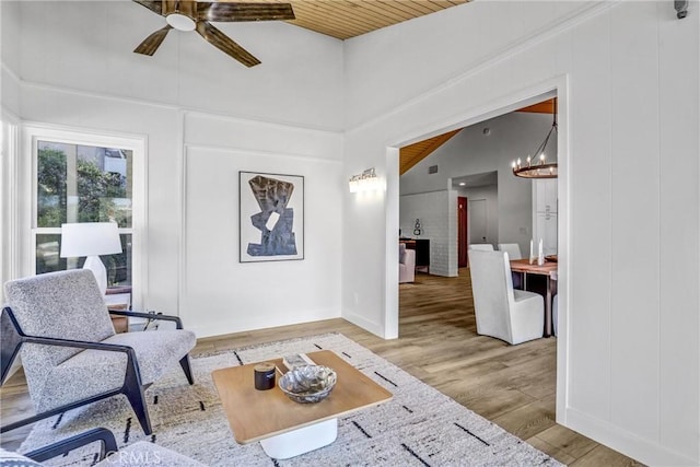 sitting room with lofted ceiling, wood ceiling, light wood-style floors, a decorative wall, and ceiling fan with notable chandelier