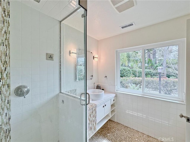 bathroom with visible vents, a stall shower, tile walls, wainscoting, and vanity