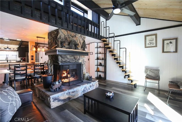 living area with a ceiling fan, wood finished floors, a stone fireplace, lofted ceiling, and stairs