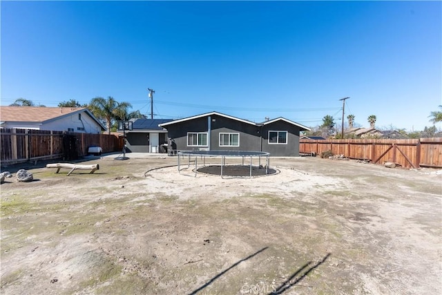 rear view of house with a trampoline and a fenced backyard