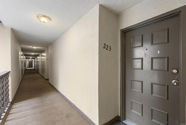 corridor featuring carpet, baseboards, a textured wall, and a textured ceiling