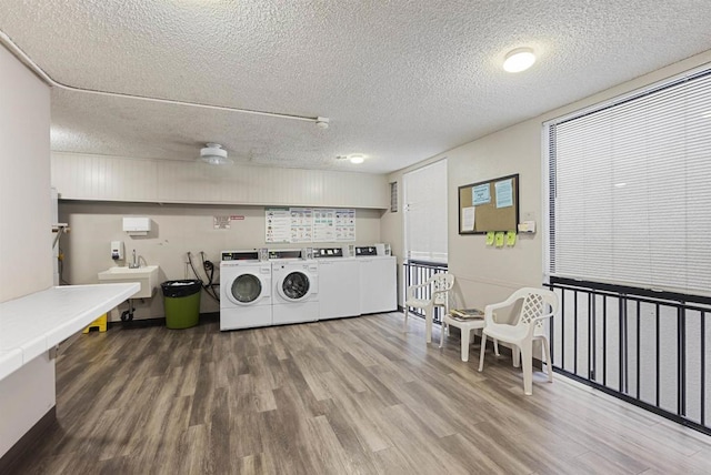 common laundry area featuring a textured ceiling, a sink, wood finished floors, and washing machine and clothes dryer