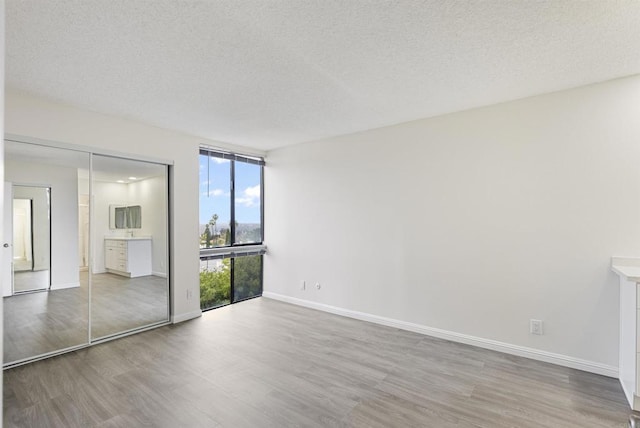 unfurnished bedroom featuring floor to ceiling windows, wood finished floors, baseboards, and a textured ceiling