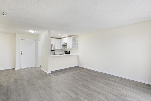 unfurnished living room with a textured ceiling, baseboards, and wood finished floors