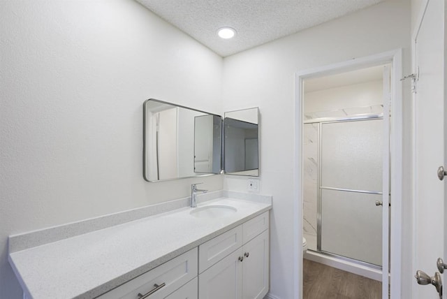 bathroom with toilet, a stall shower, wood finished floors, a textured ceiling, and vanity