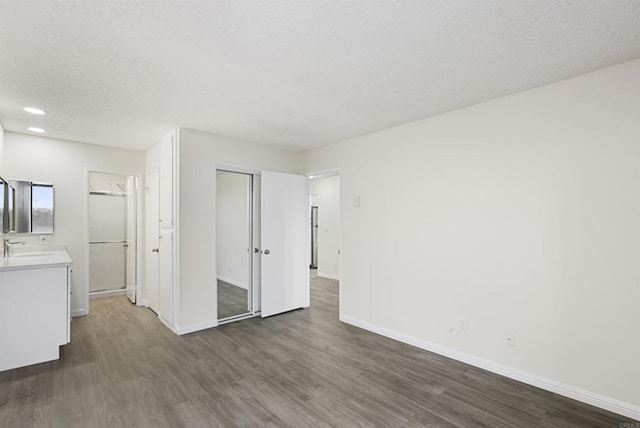 unfurnished bedroom with a sink, a textured ceiling, dark wood-style floors, a closet, and baseboards