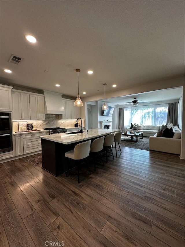 kitchen with visible vents, custom exhaust hood, a sink, white cabinets, and dobule oven black