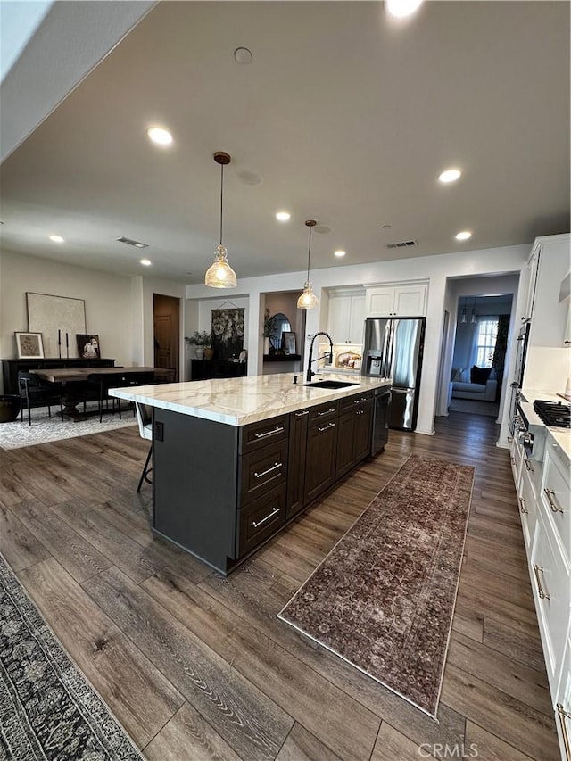 kitchen with dark wood-style floors, an island with sink, a sink, white cabinetry, and stainless steel fridge