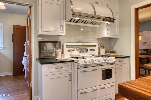 kitchen featuring range with two ovens, decorative backsplash, dark countertops, and range hood