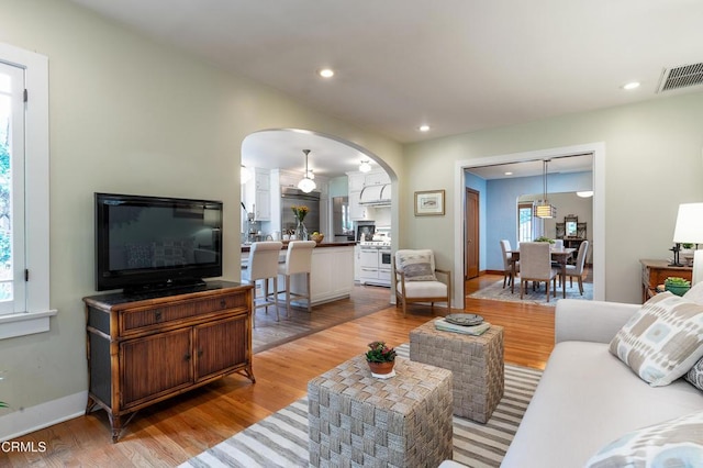 living room featuring light wood-style floors, recessed lighting, visible vents, and arched walkways